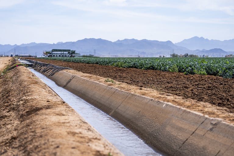 A scenic view of an irrigation canal running through farmland with mountains in the background.